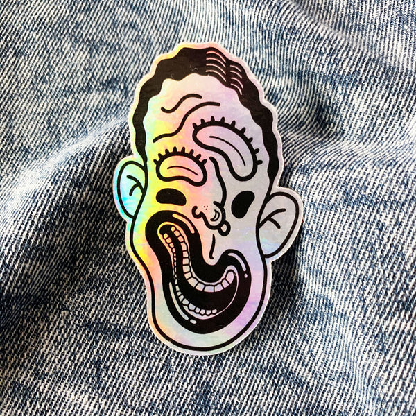 Squiggly face in black and white on holographic sticker vinyl with a gloss finish that is waterproof, UV-resistant, and able to withstand excessive handling. From Osseous Design by independent artist Makena Peet.
