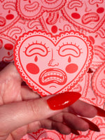 Crying, red heart-shaped face, vinyl sticker with matte finish. Scratch, water, and sunlight resistant. From Osseous Design by independent artist Makena Peet.