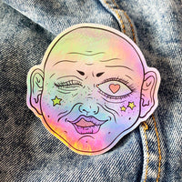 Funky pink face on holographic sticker vinyl with a gloss finish that is waterproof, UV-resistant, and able to withstand excessive handling. From Osseous Design by independent artist Makena Peet.